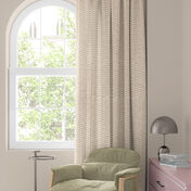 Ventana con cortina floral colorida en rojo, naranja y azul, sill&oacute;n verde y mesita con l&aacute;mpara